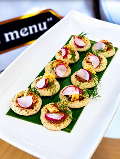 Canapés topped with sliced radish and fresh herbs on a white serving platter