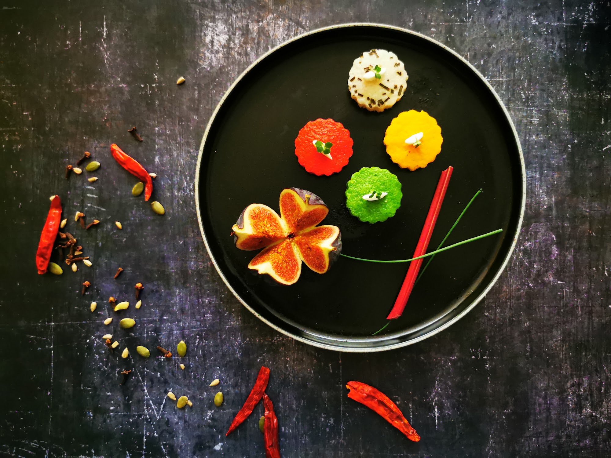 Colourful bite-sized dishes and fresh fig arranged on a black plate