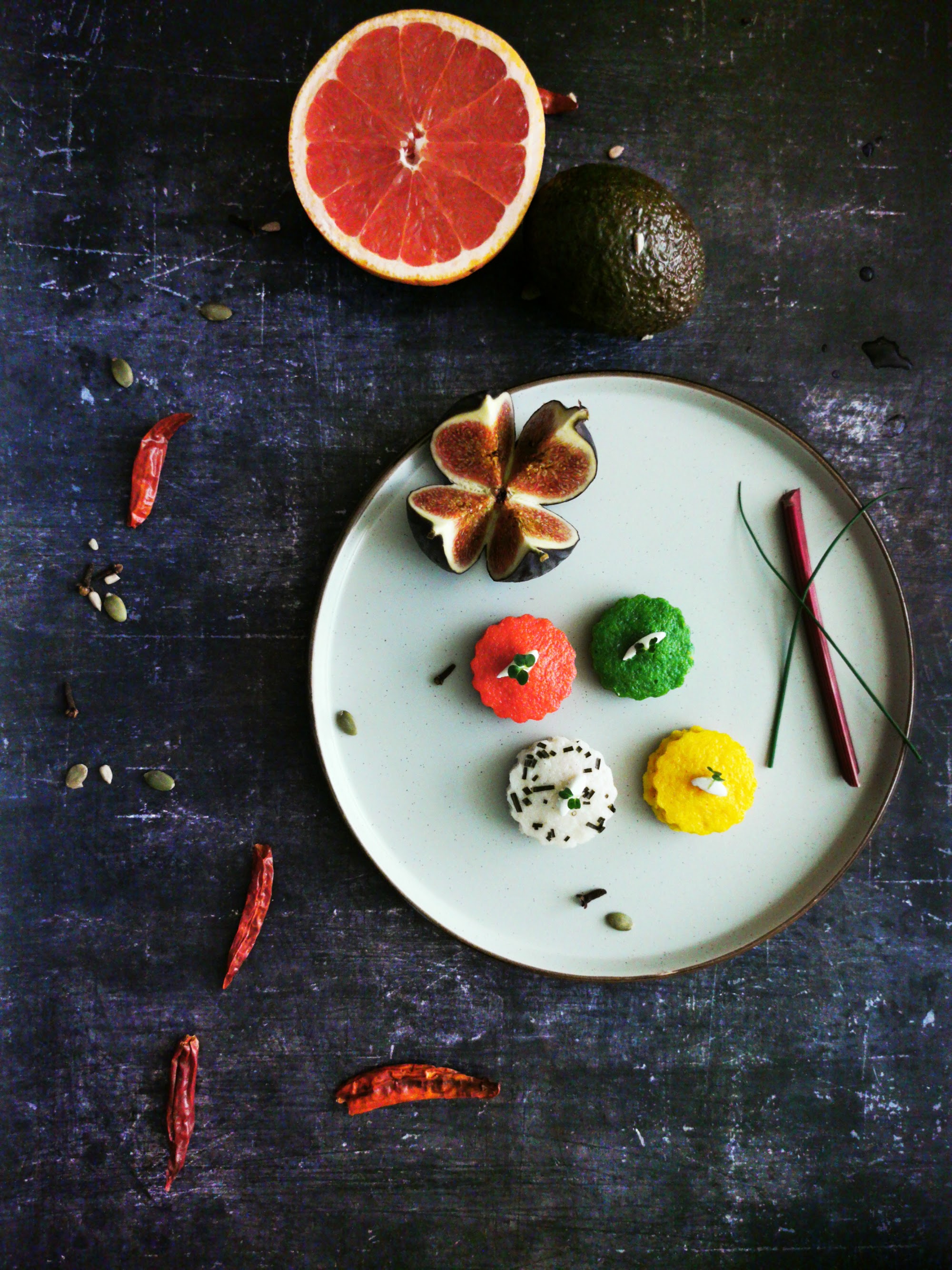 Four colourful bite-sized dishes on a white plate with fresh fig and spices